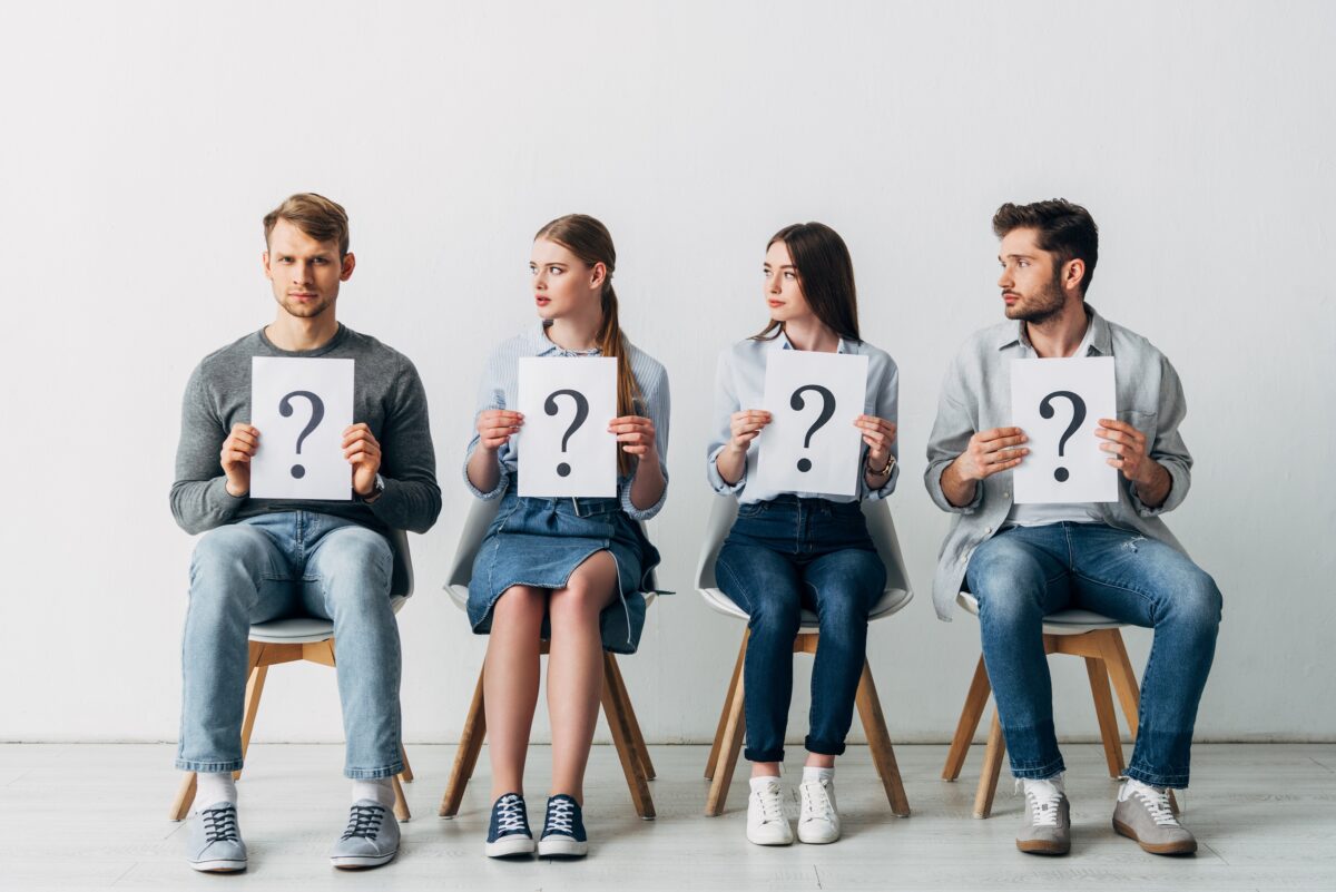 Man,Looking,At,Camera,Near,Employees,Holding,Cards,With,Question